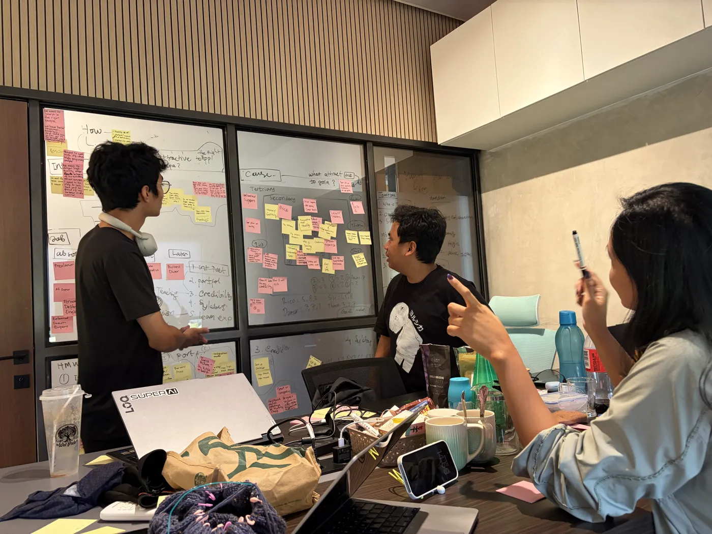 Tim membedah brief di depan papan penuh sticky notes